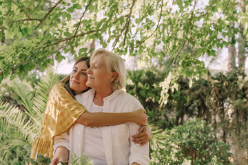 Loving daughter embracing mother while standing against plants in yard
