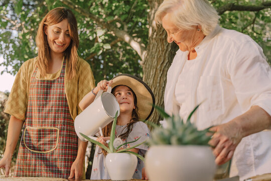 Smiling mother and grandmother looking at girl watering potted plant in yard