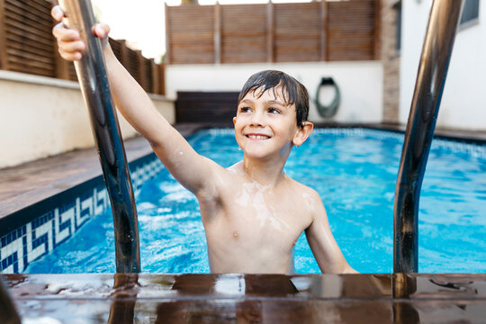 Smiling boy holding ladder in swimming pool