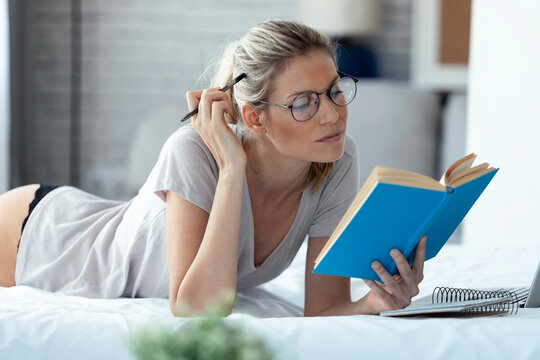 Blond woman reading a book lying in bed