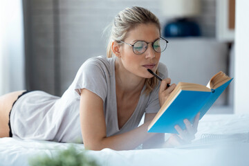 Blond woman reading a book lying in bed
