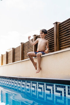 Boy flexing muscles while sitting at poolside