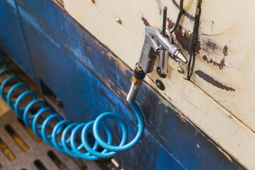 air gun with blue spiral hose hanging on a metal hook in a workshop foreground focus