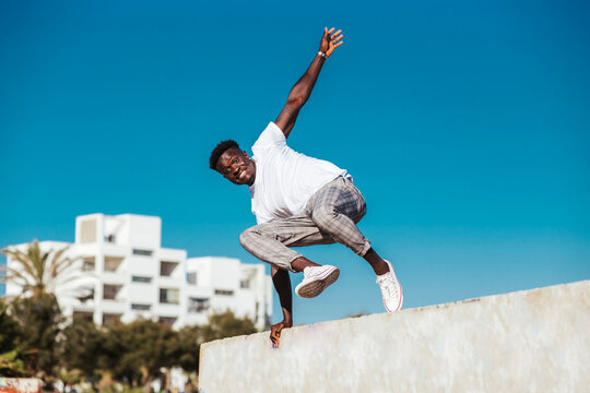 African man jumping over retaining wall against clear blue sky during sunny day