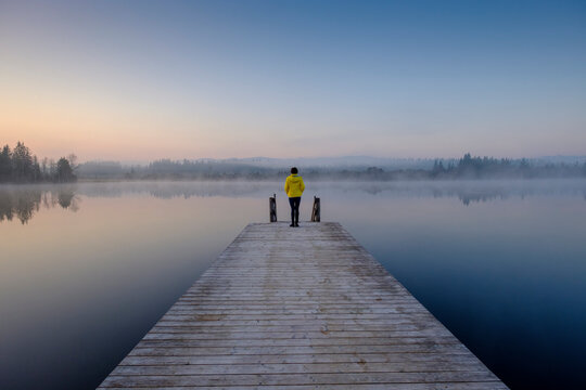 Woman standing at edge of lakeshore jetty at foggy dawn