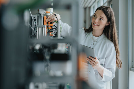 Smiling female scientist holding digital tablet inventing machinery in laboratory