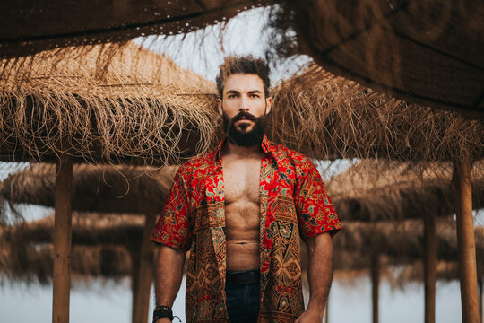 Attractive bearded man with colorful shirt standing between beach umbrellas
