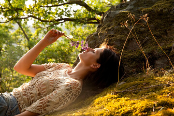 Young woman lying in forest smelling at bunch of flowers
