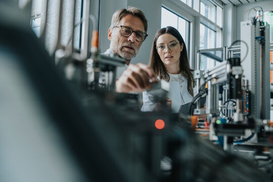 Male scientist with young woman examining machinery in laboratory - Powered by Adobe