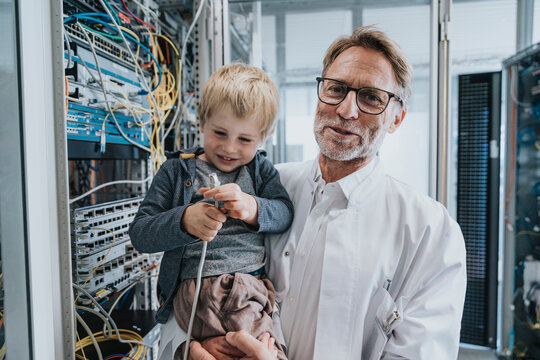 Male IT professional carrying son while standing by network server in data center