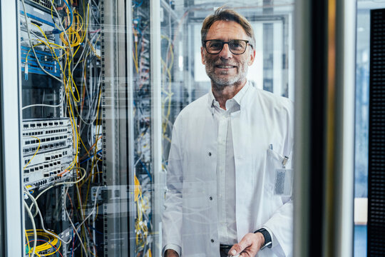 Male IT professional standing by network server in date center seen through glass