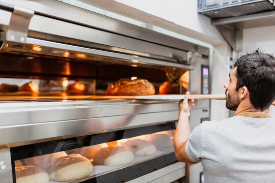 Baker baking bread in oven at bakery
