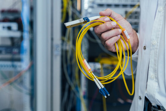 Close-up of mature man holding yellow cables in data center