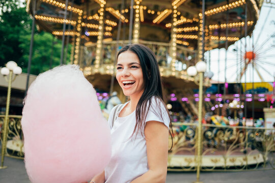 Cheerful young woman with cotton candy standing in amusement park