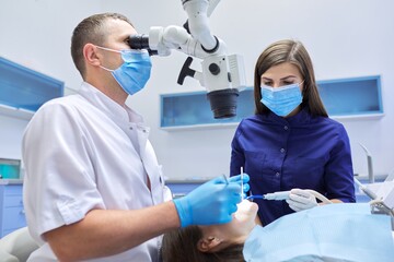 Male doctor dentist treating teeth using dental microscope instruments