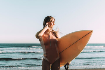 Young woman with surfboard looking away while standing against sea during sunset