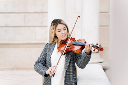 Blond young woman playing violin in city