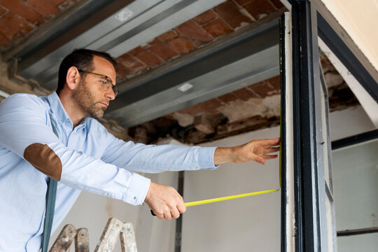 Architect using tape measure on window frame in a house under construction