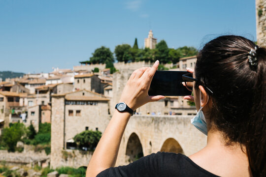 Woman wearing protective mask and taking a photo with her smartphone of Besalu, Catalonia, Spain