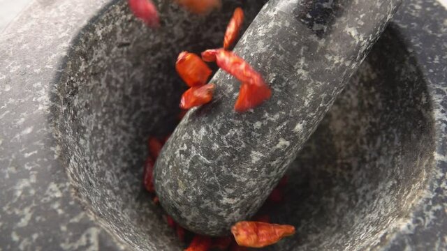 Close-up of red cayenne pepper pods falling into the stone mortar in slow motion