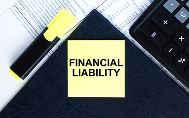 Yellow sticker with text Financial Liability laying on the folder with yellow marker and calculator