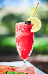 Icy Raspberry Lemonade in Tall Glass with Lemon Wedge and Black Berry with Outdoor Blurred...