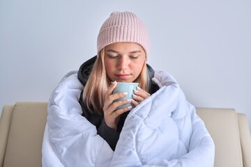 Cold autumn winter season, teenage girl sitting on sofa under warm blanket