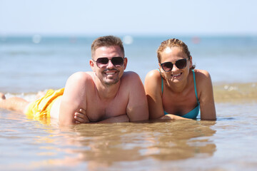 Couple sunbath in sun. Man and woman in sunglasses lie side by side in water.