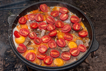 Scrambled eggs with tomato slices in a large flat skillet, outdoor.