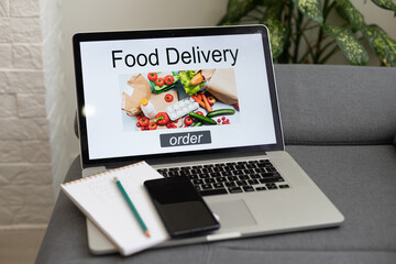 ordering food online concept: woman with a laptop showing fast food website on screen. Screen graphics are made up.