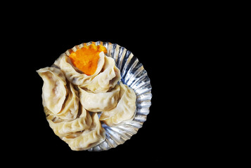 a plate of chicken momo with chilli sauce in a silver foil plate in black background.