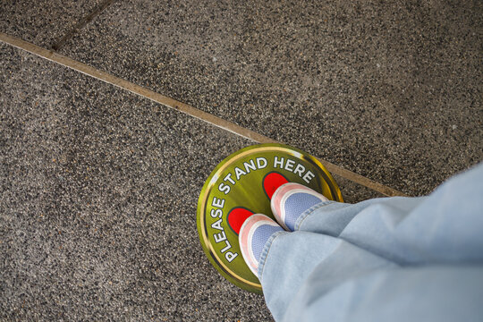 Top view of feet standing in red circle with text in public space practicing social distancing.