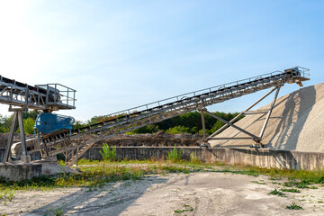 A system of interconnected conveyor belts over heaps of gravel against a blue sky at an industrial cement plant.
