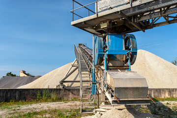 A system of interconnected conveyor belts over heaps of gravel against a blue sky at an industrial cement plant.