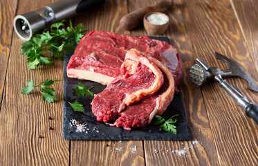 Raw beef fillet whole piece and two slices on wooden boards, meat tenderizer hammer, parsley and salt with spices