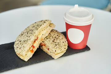 A sandwich with a red plastic glass of coffee on the table in a coffee shop. High-quality photo. Close-up