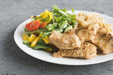 Cooked turkey breast, vegetable salad with cherry tomatoes, yellow bell pepper, cucumber and arugula, whole wheat fusilli pasta. Balanced meal concept