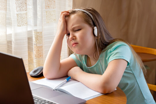 Distance learning online education. Photo of little upset and boring pupil. Little cute girl is bored and tired with doing her homework. New normal. Social distancing.