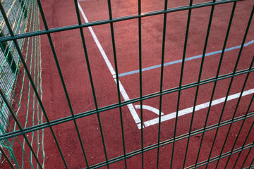 Close-up of white marking lines of outdoor basketball court fenced with protective metal fence.