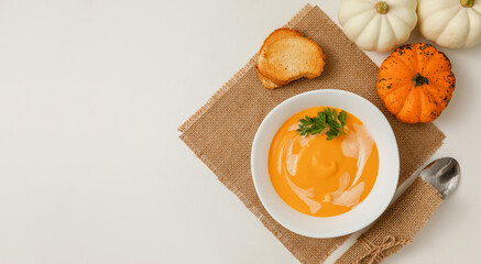 A bowl of pumpkin or carrot vegetarian cream soup is garnished with fresh parsley and cream on a white textured table. flat lay, copy space