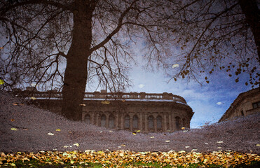 Fototapeta na wymiar The old building is reflected in a puddle, autumn leaves lie around