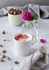 Pink moon milk with rose petals in white mug, healthy Ayurveda drink. Fresh rose and dried rose buds