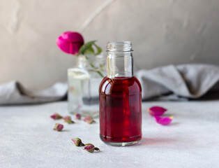 Rose essence in bottle and fresh rose on grey concrete background