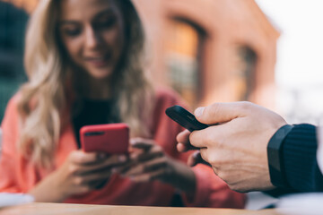 Crop man and woman using smartphone in street cafe