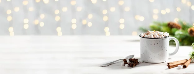Selbstklebende Fototapeten Christmas banner with white cup with hot chocolate and marshmallows on with cinnamon sticks with garland lights © Olga Krivokoneva