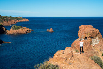 vue panoramique sur une mer bleu azur et une côte de rochers rouges et un marcheur 