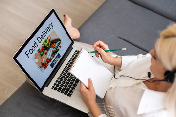 ordering food online concept: woman with a laptop showing fast food website on screen. Screen graphics are made up.