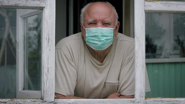 Portrait Of Adult Caucasian Man In Protective Medical Mask Looking Out Of Window