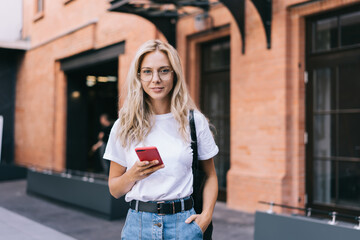 Smiling woman in eyeglasses messaging on smartphone on street