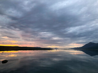 Beautiful spring night with the last rays of the sun over the sea reflecting in the water in Norway. The sun crossing the horizon with silhouette of mountains and its accompanying atmospheric effects.